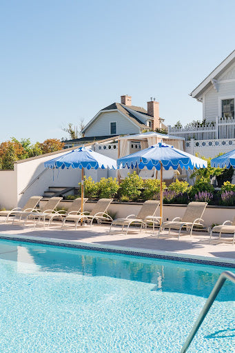 View of a tranquil outdoor pool at a Hamptons spa with blue umbrellas and lounge chairs, offering a serene environment for relaxation.