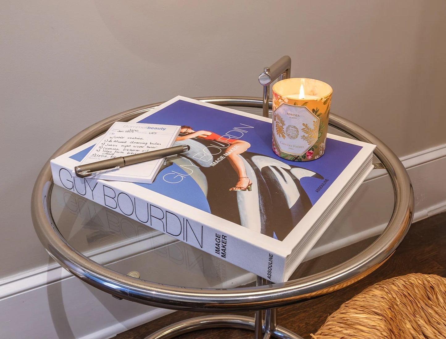 An aesthetic setup of a coffee table book with a candle, a small notepad, and a pen.